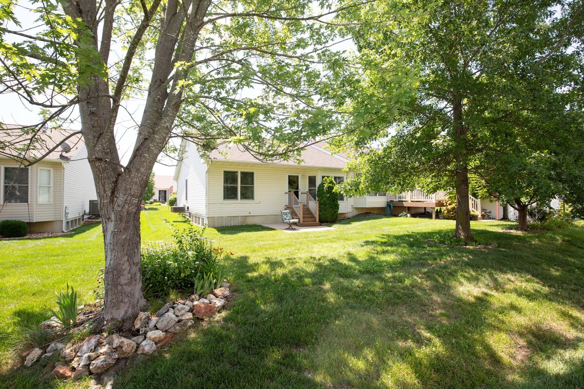Exterior photograph of a home, from the back of the yard looking at the back right corner of the house. There are large trees on both sides.