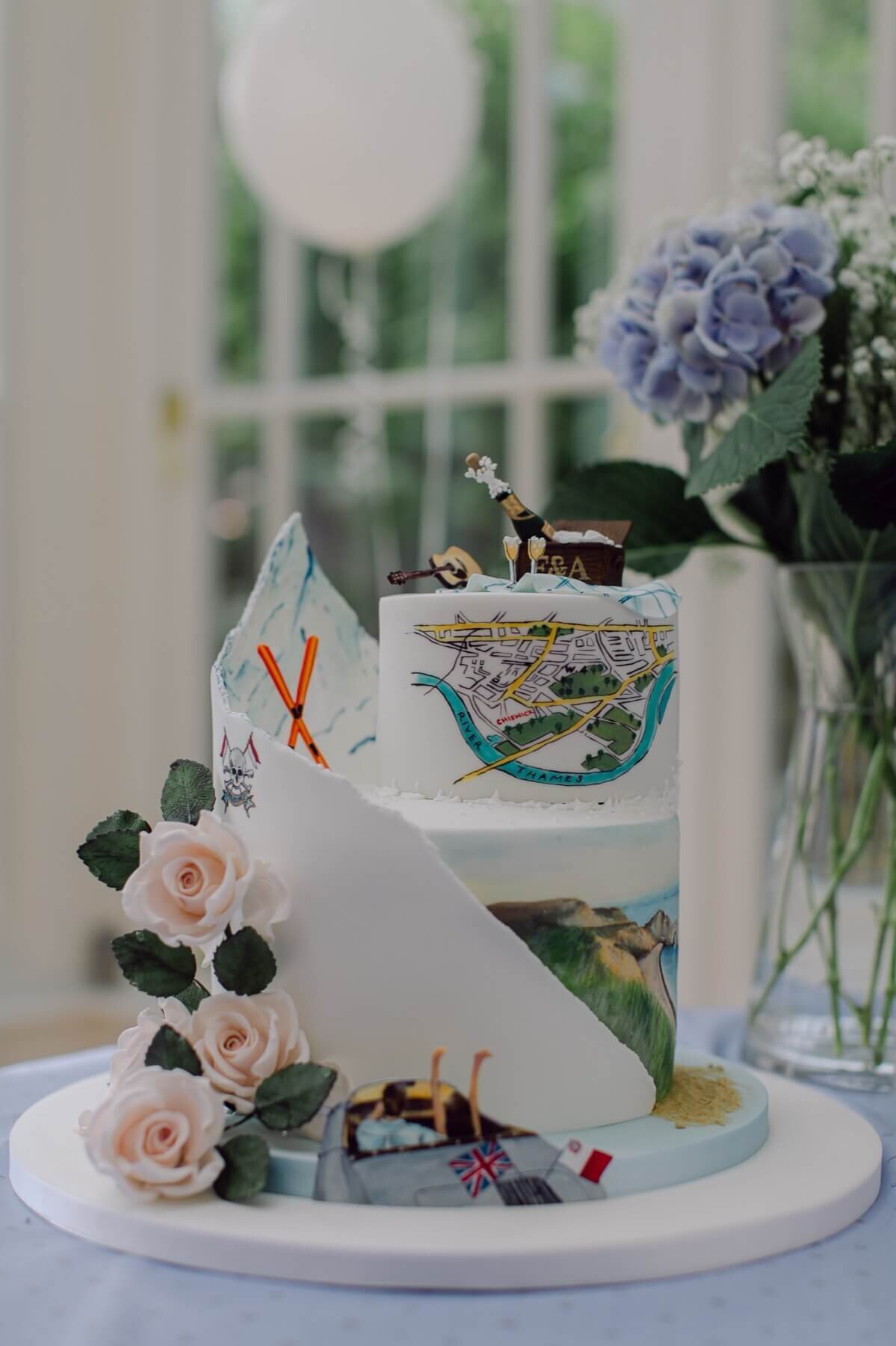 A unique wedding cake with 2 tiers. The cake includes a hand painted map, a chapagne bottle, a guitar and rose sugar flowers