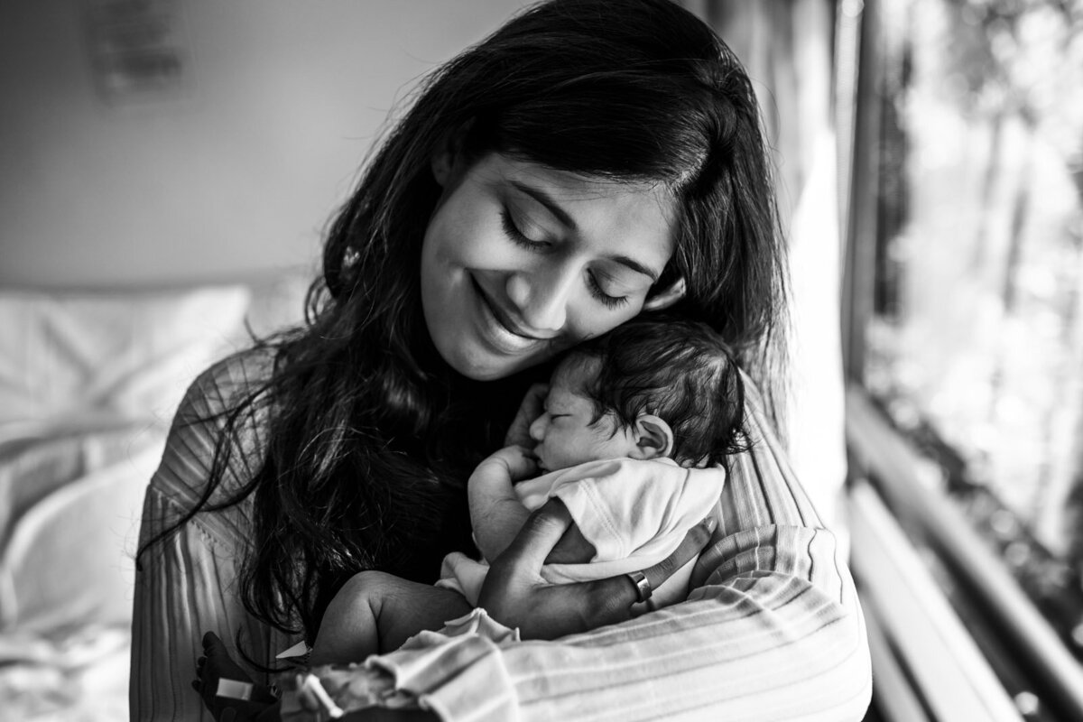 mom smiling and holding newborn close to her face in hospital room