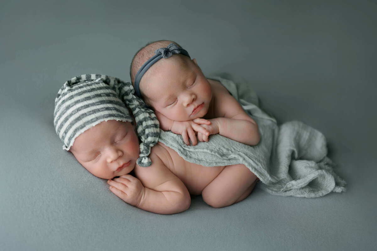 twin newborns laying on eachothers backs on a blue backdrop at their newborn session