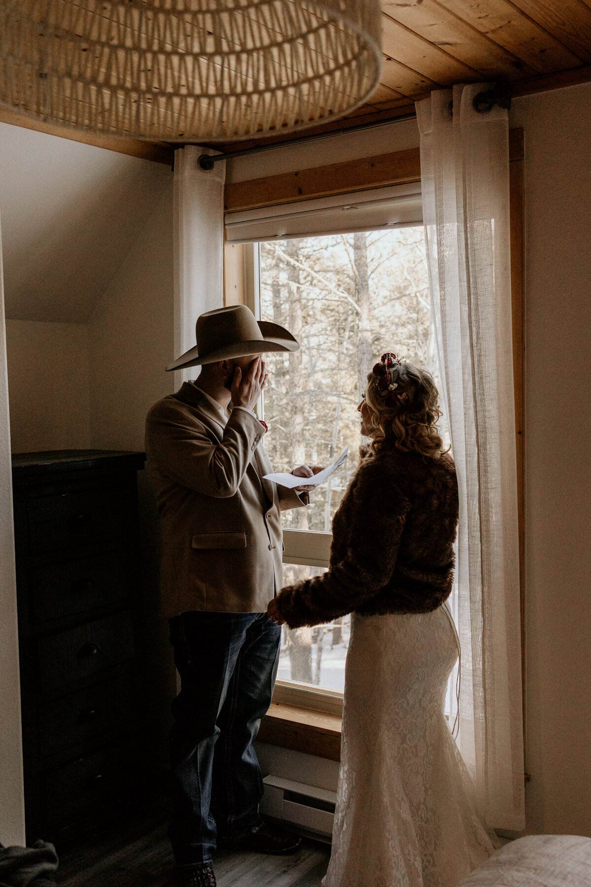 bride and groom exchanging personal vows in front of a window in a cabin