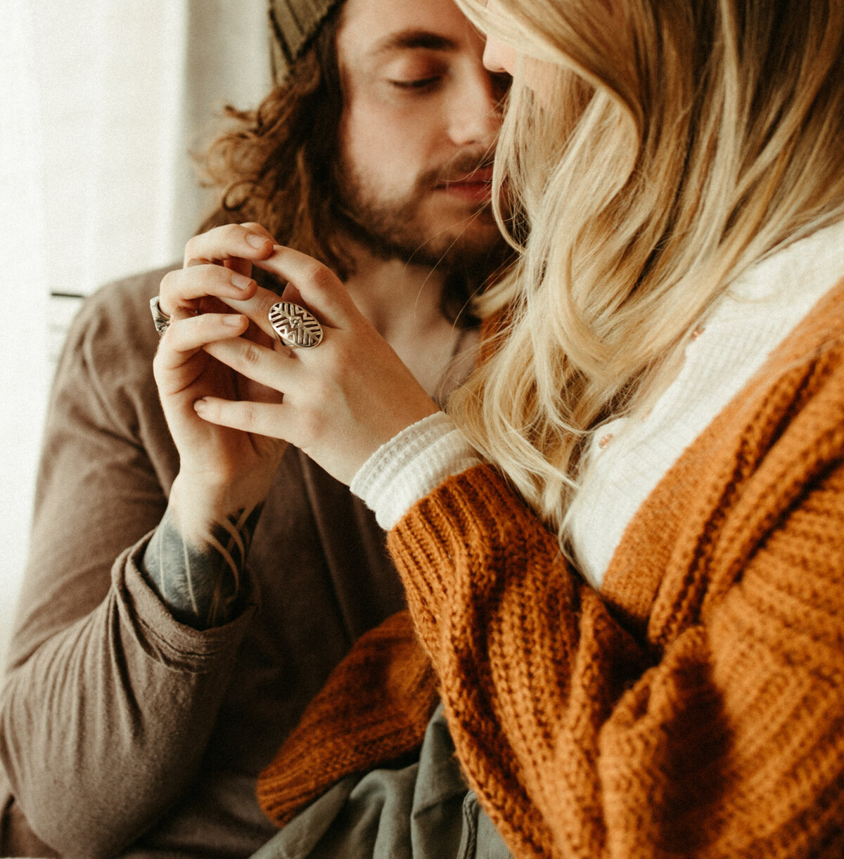 Couple in cozy sweaters sitting beside window holding hands