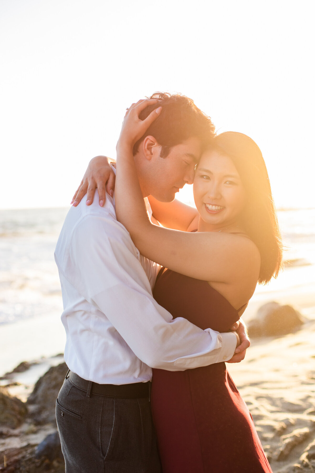 engaged couple nuzzle and smile at sunset