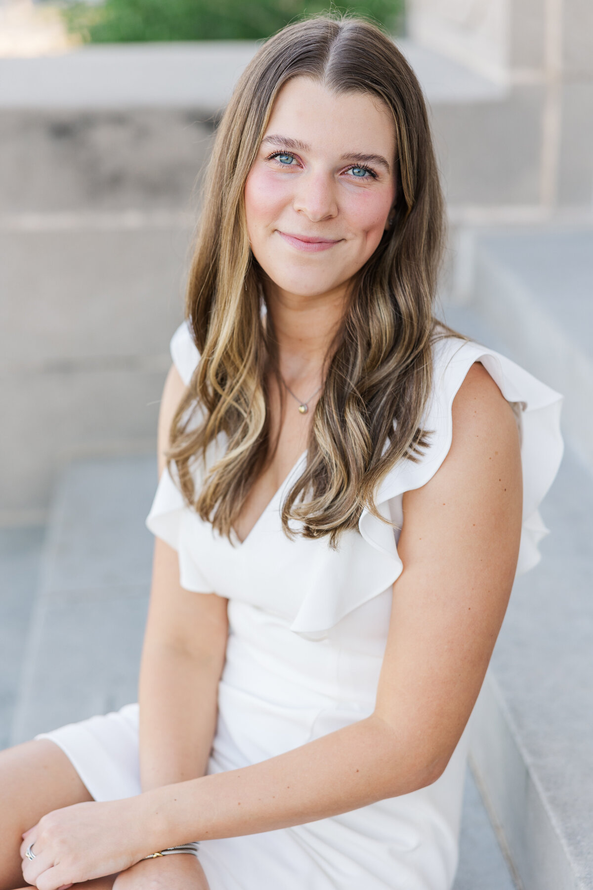 Natural light senior photo of an Aggie graduate in a white dress seated on the steps at Texas A&M University in College Station, TX.