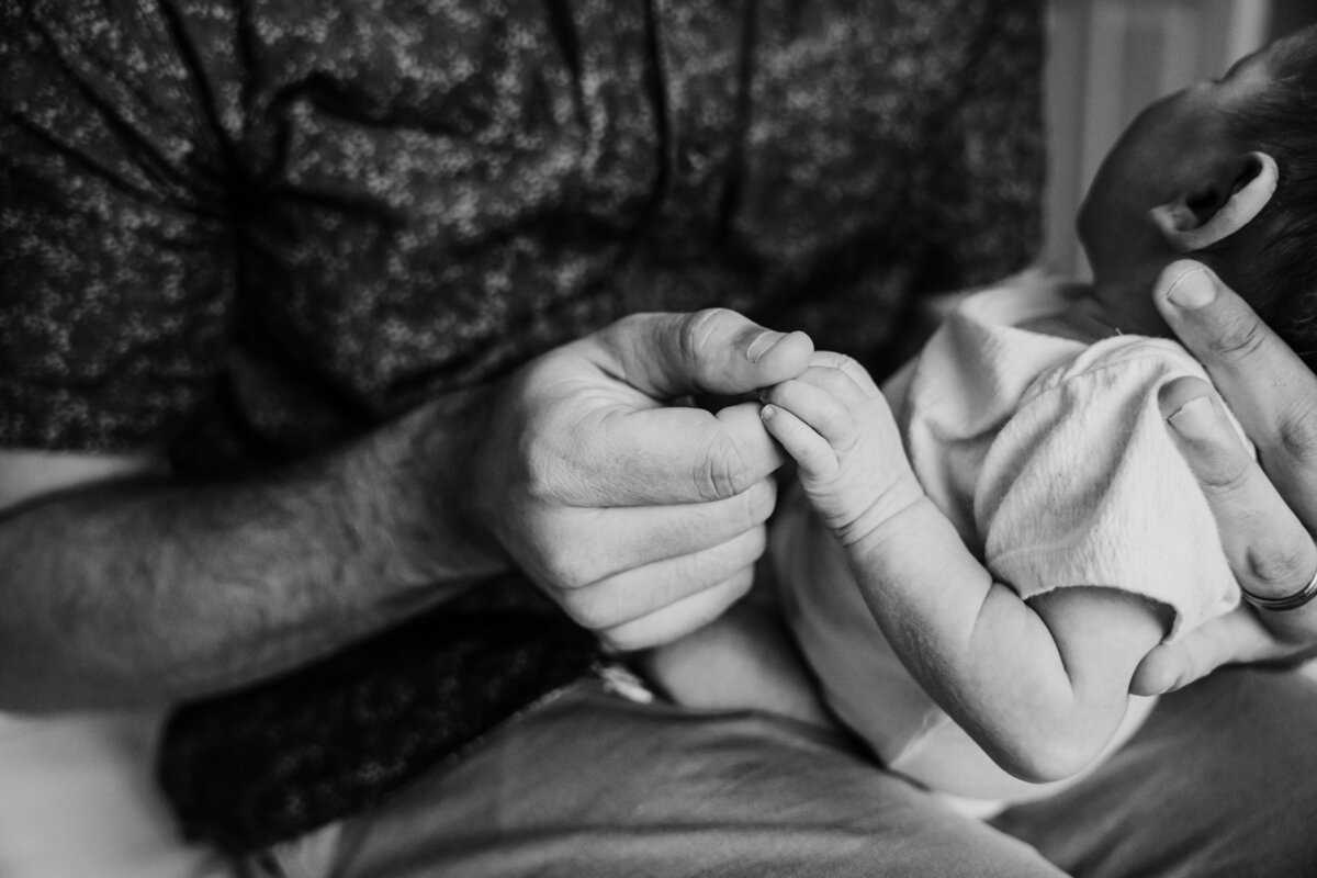 Newborn Photographer, a father's hands hold his baby on his lap