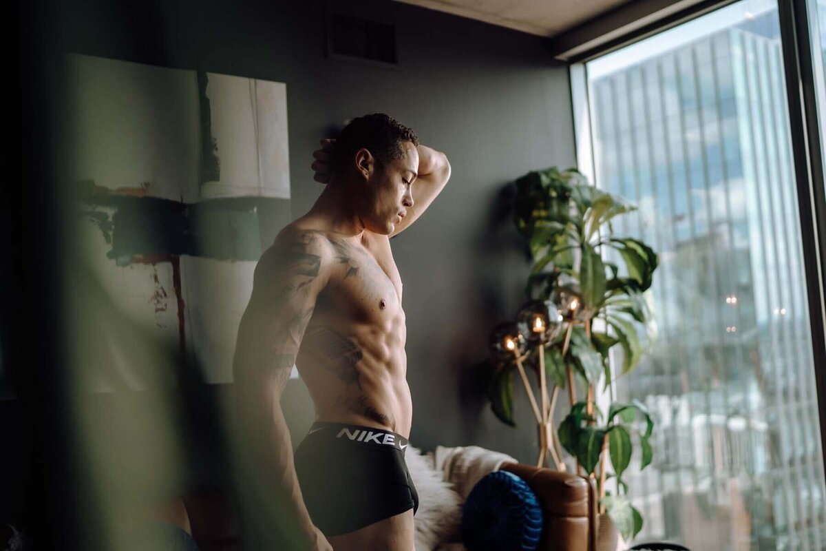 Masculine boudoir portrait of man looking out of the window of Nashville high rise