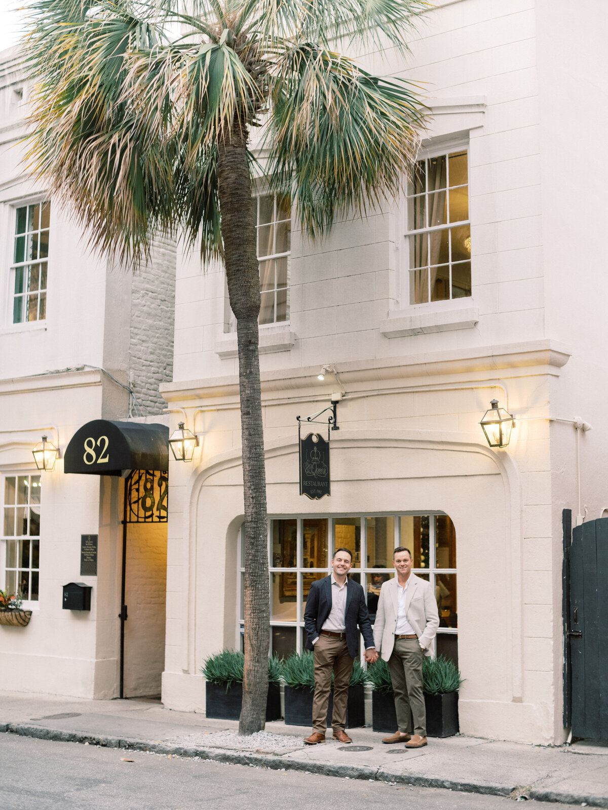 A stylish couple poses in front of a charming building in Charleston, embodying elegance and fashion, framed against an inviting backdrop that showcases their sophistication.