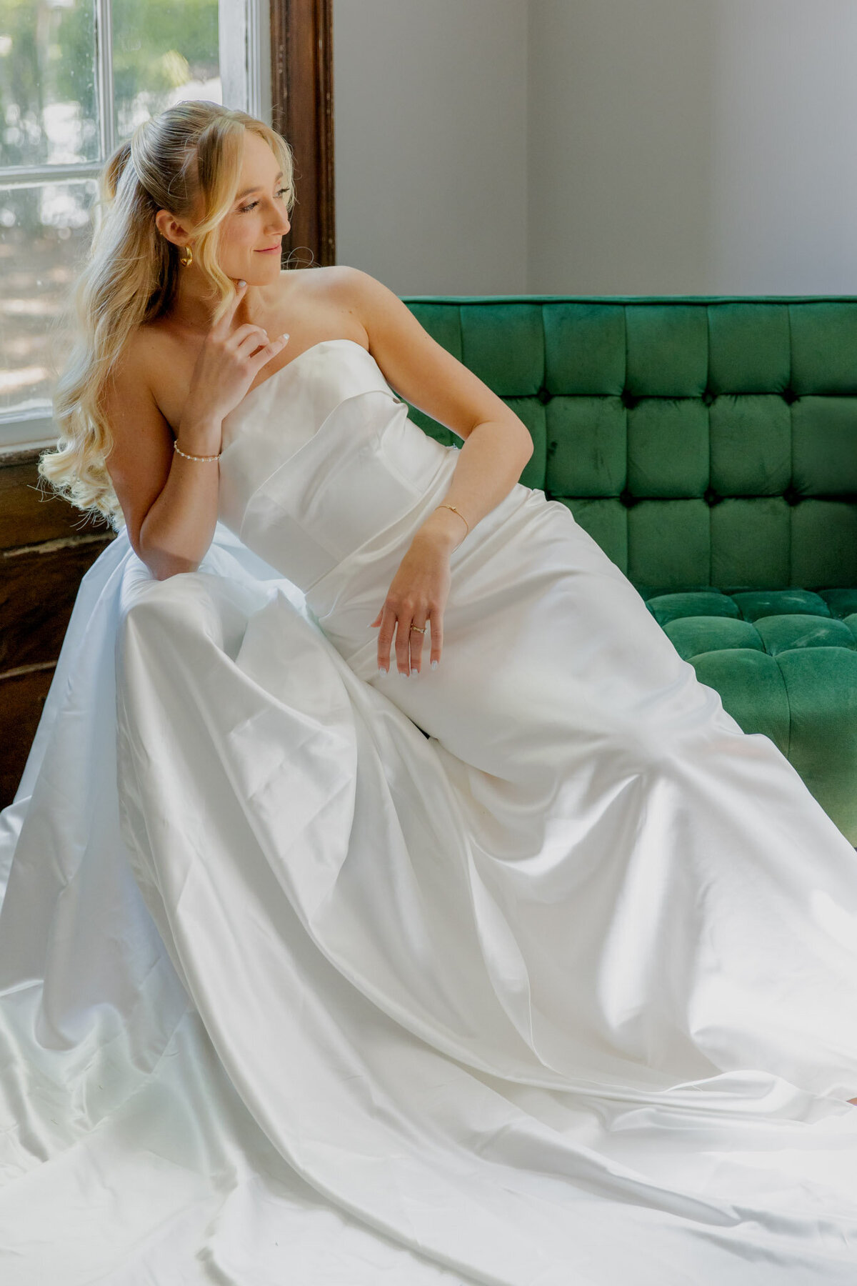 A bride sits, almost laying on a lush, forest green couch inside of a house. The photo is cropped so you can't see above her nose.
