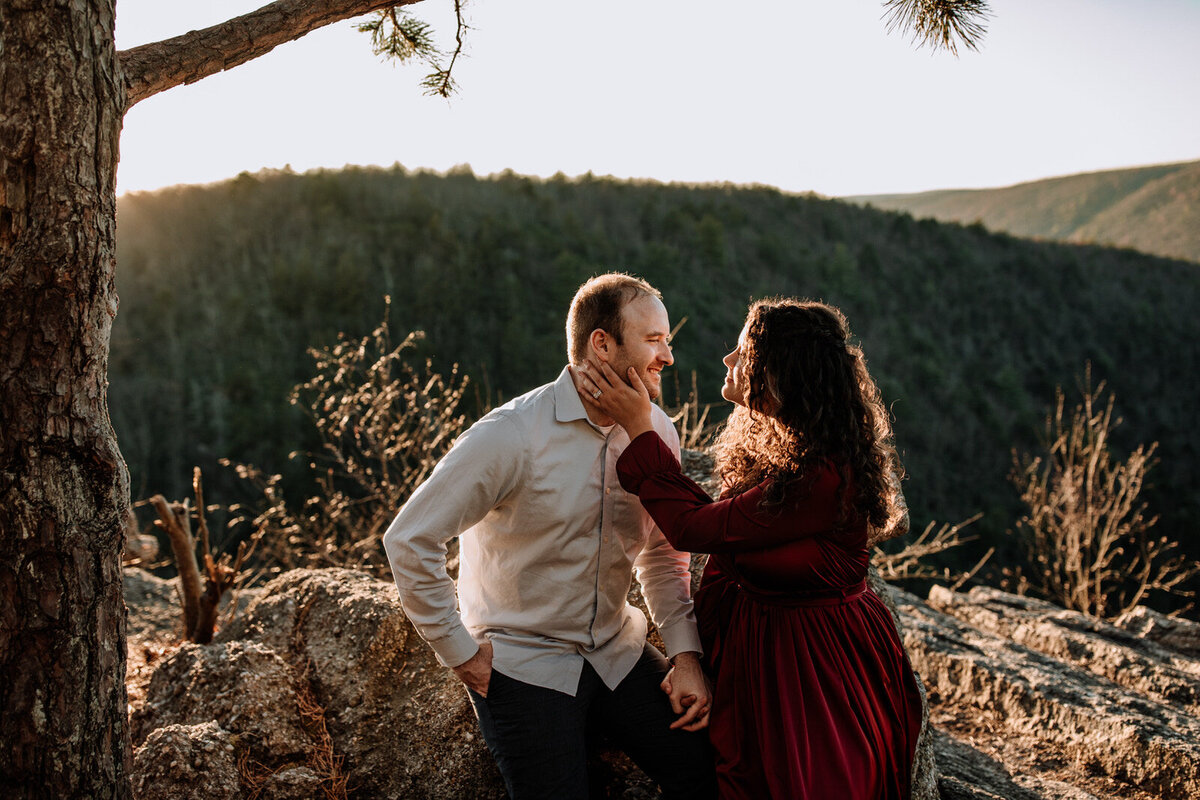 Bride and groom holding hands looking at each other while standing in front of rolling hills with the sunlight coming down on them