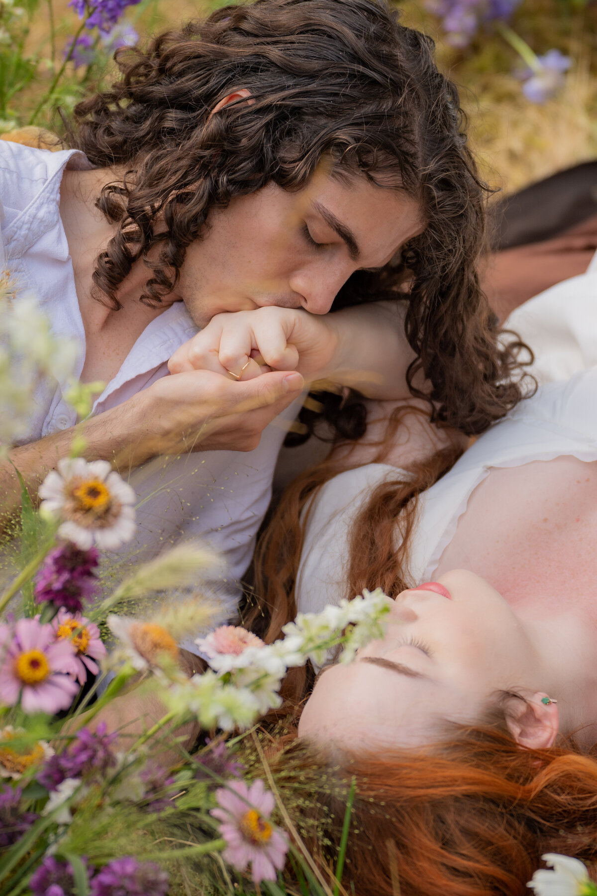 A person laying next to their partner as they kiss their hand.