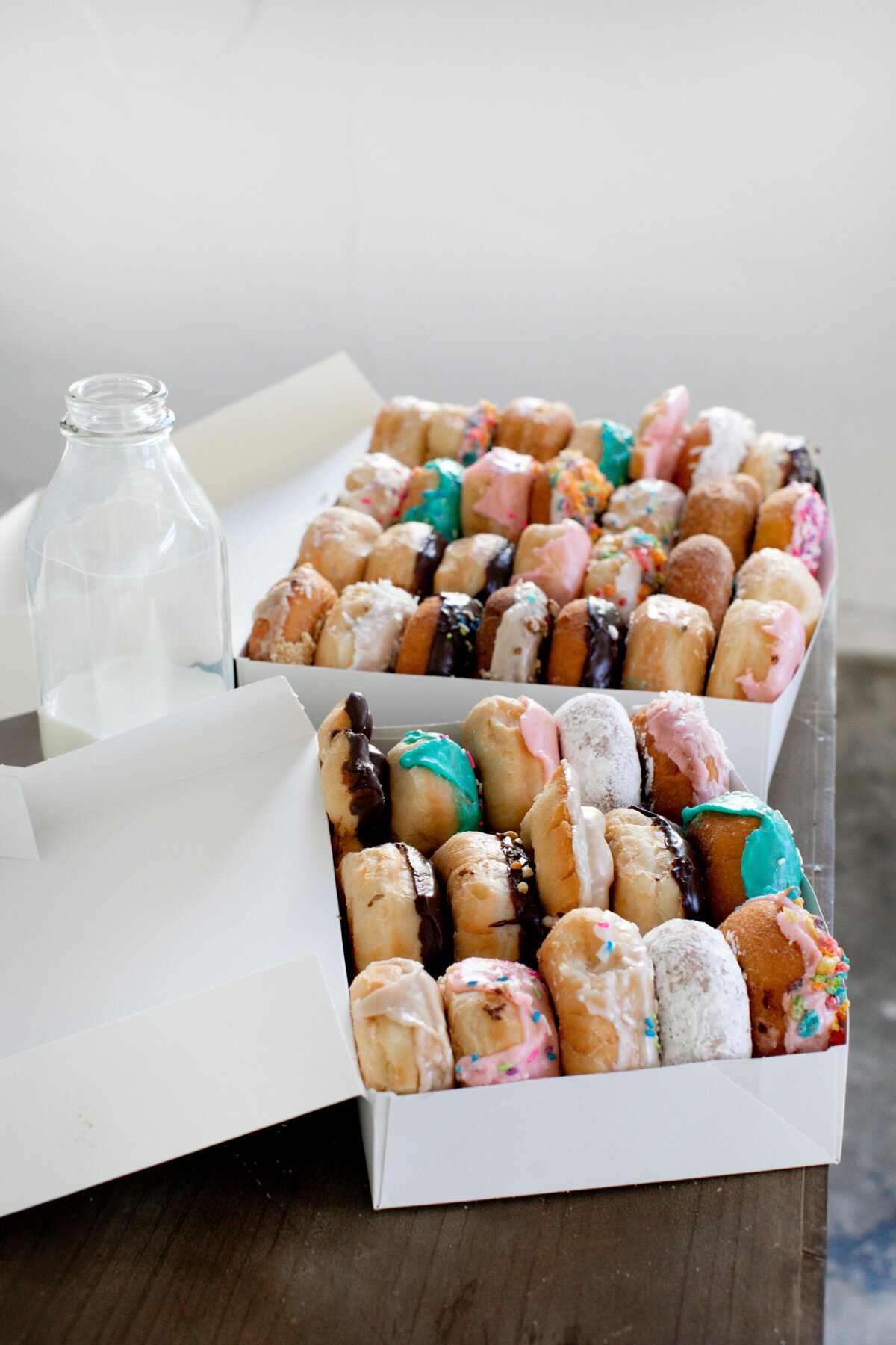 Milk Jug and Stacked Donuts in a Box  on a Table - Daylight Donuts