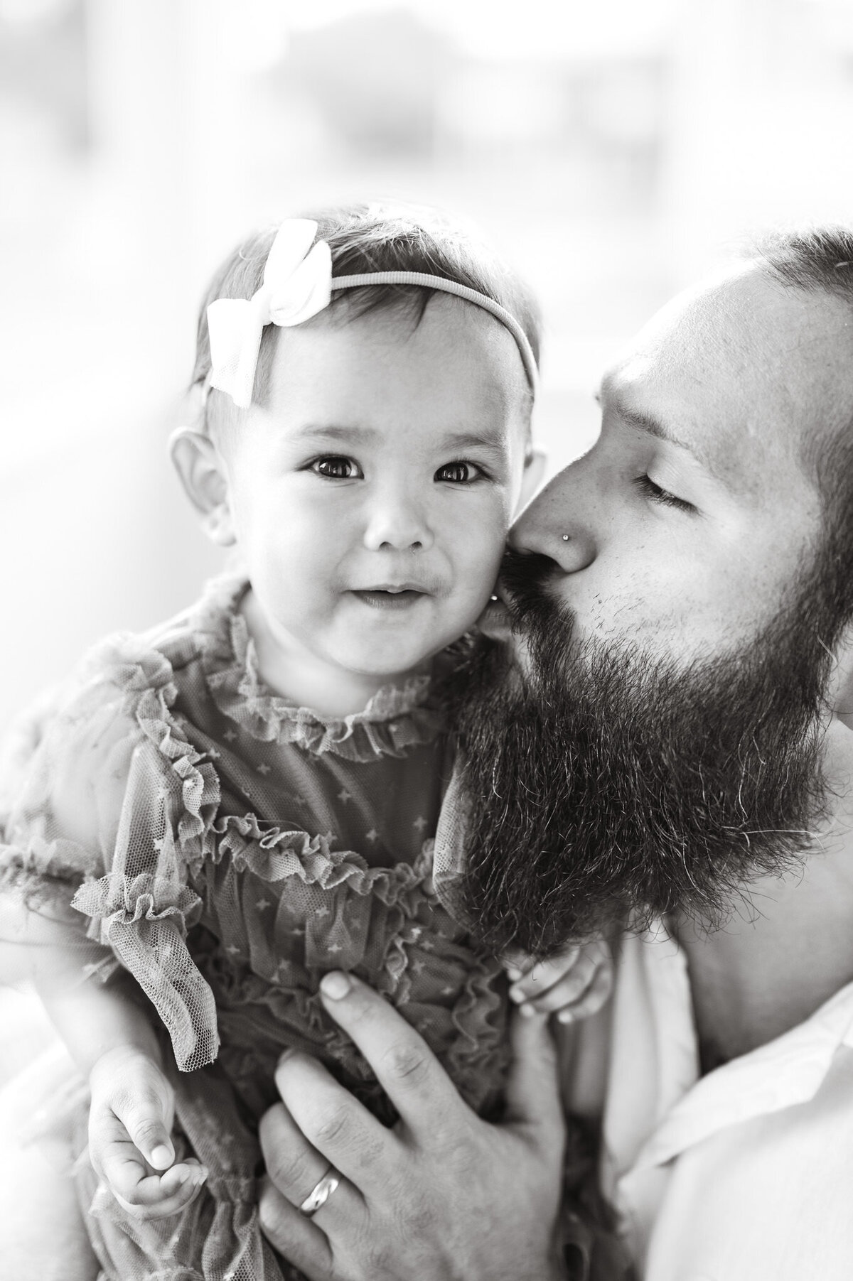 Black and white image of a dad kissing his little girl on the cheek.