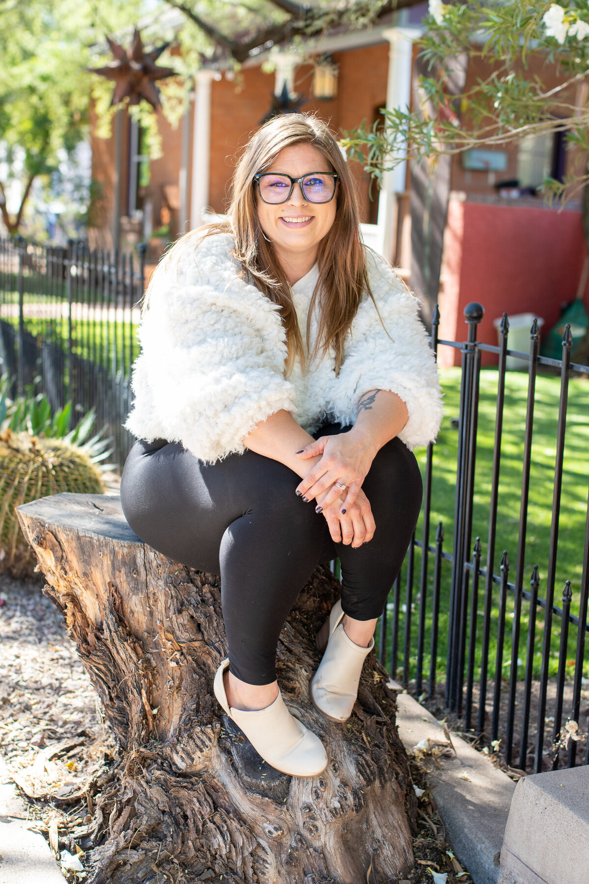Smiling woman in a white textured sweater sitting on a tree stump outdoors, photographed by Vyrl Photo, showcasing Tucson brand photography.