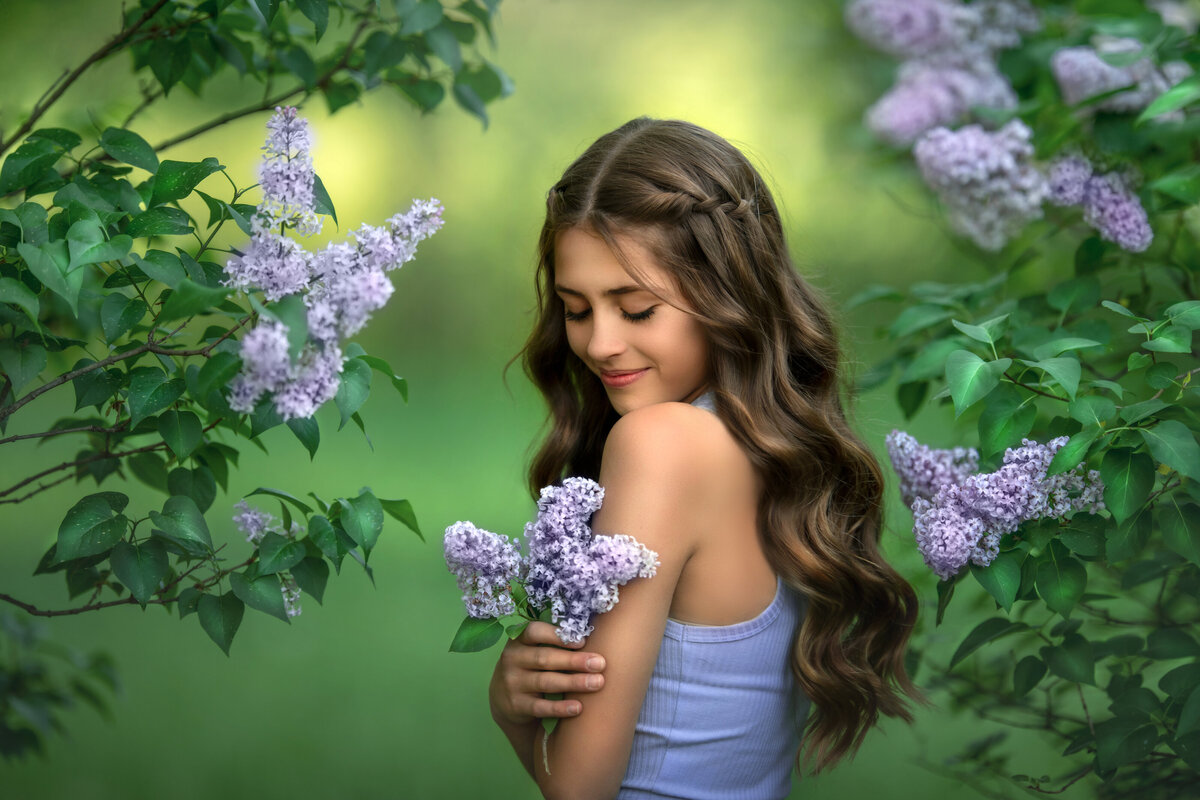 Long hair Brunette girl surrounded by lilac bush in purple tank top in the spring.