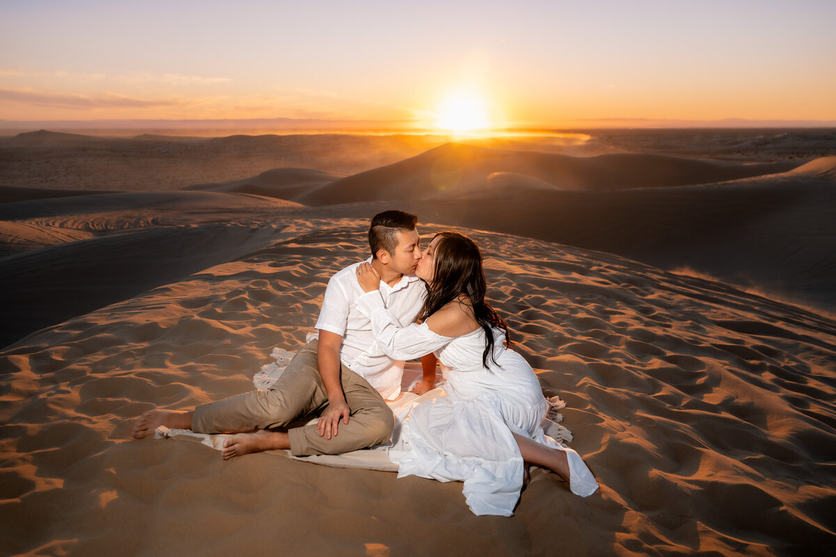 Glamis Sand Dunes elopement bride and groom during sunset sitting on blanket and kissing.