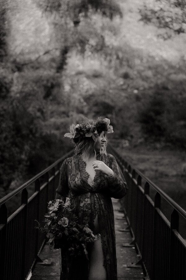 Portrait noir et blanc d'une future mère sur un pont, bouquet à la main et couronne de fleur sur la tête. Par Kamescop vidéaste et photographe en Bretagne.