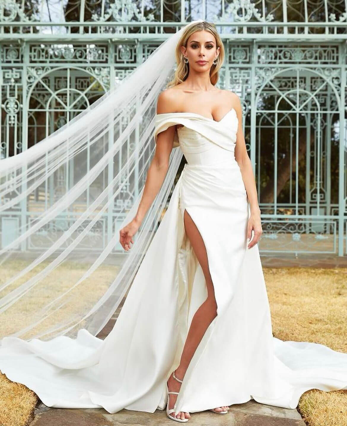 This stunning bride showcases timeless Hollywood waves and flawless wedding makeup to complement her off-the-shoulder gown with a dramatic slit. The flowing veil and elegant earrings complete this show-stopping bridal look. Perfect inspiration for brides seeking a luxury hair salon or mobile makeup artist in Austin or San Antonio. Mistique Makeup provides expert wedding hair and makeup styling, specializing in mobile bridal services and glamorous looks for modern brides.