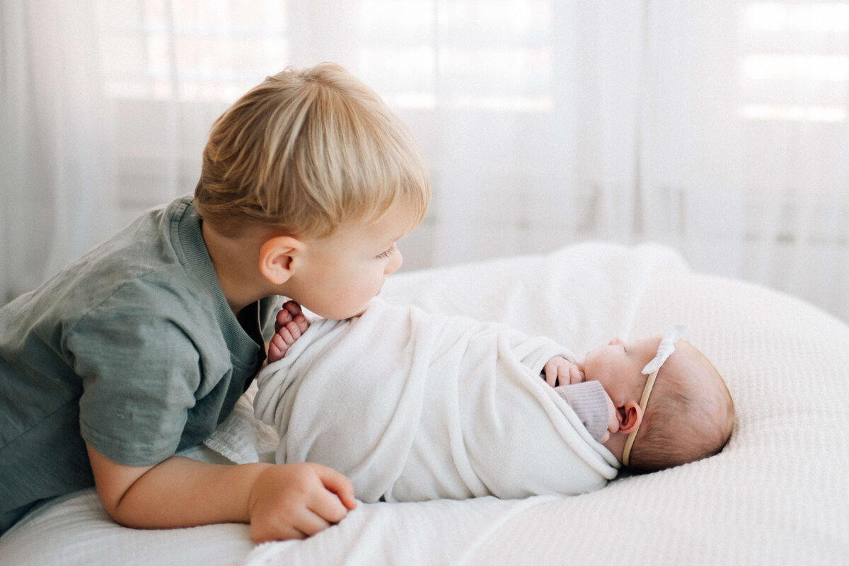 profile photo of big brother looking at baby sister who is swaddled with her feet poking out