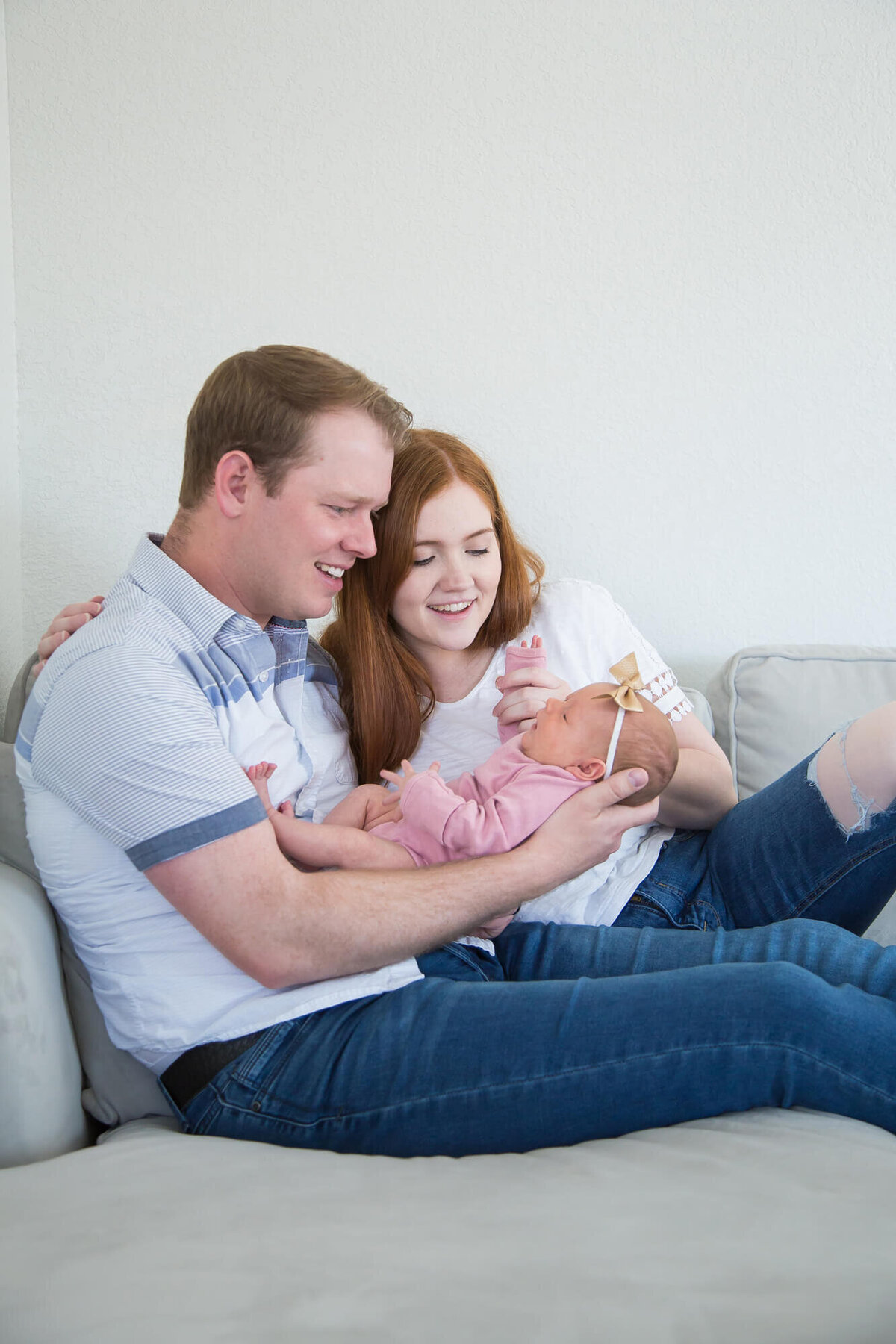 joyful couple playing with newborn baby girl on couch during las vegas newborn photography session with Jessica Bowles