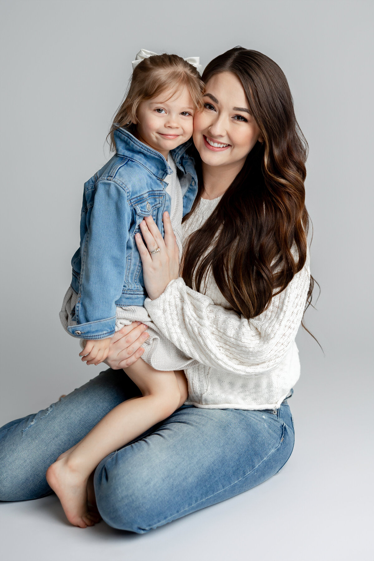 Mother holding daughter on her lap in soft natural light studio. Photographed by Yucaipa family photographer Kaitlyn Dawn Photography.