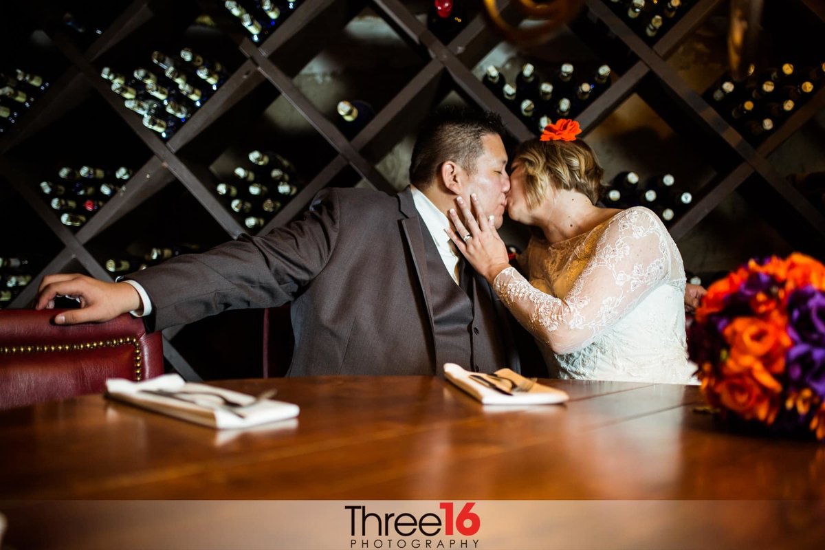 Bride and Groom share a tender kiss in front of the wine bottle wall