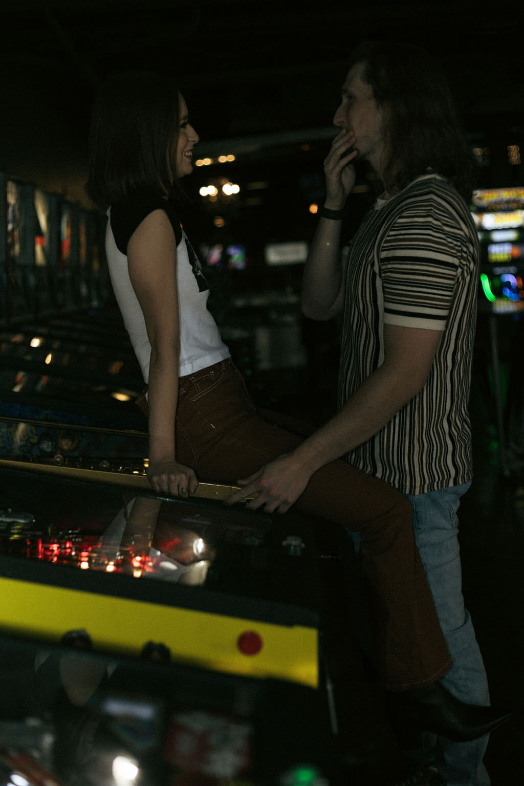 A person sitting on a pinball machine with their partner in front of them.