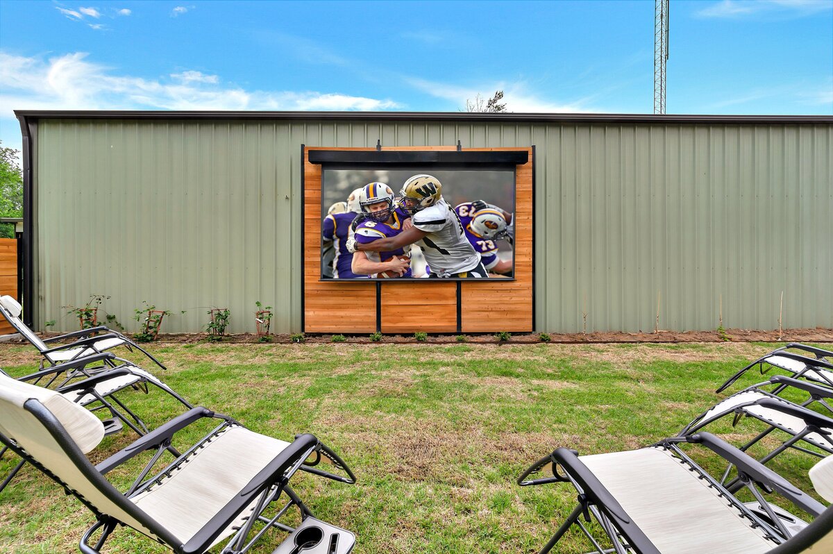 Backyard entertainment area with outdoor projector at this three-bedroom, three-bathroom vacation rental home with free wifi, outdoor theater, hot tub, propane grill and private yard in Waco, TX.