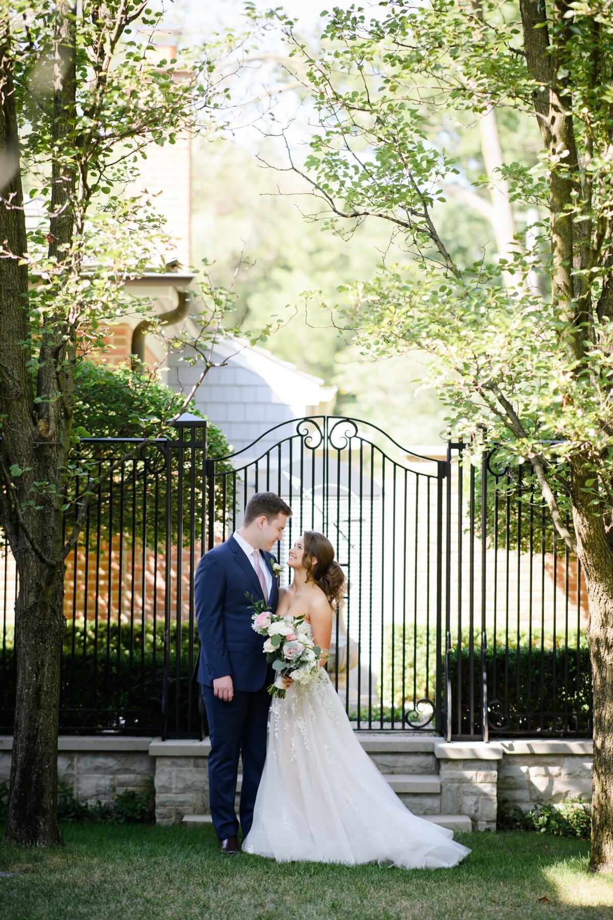 Portrait of bride and groom posed in front of a gate surrounded by trees