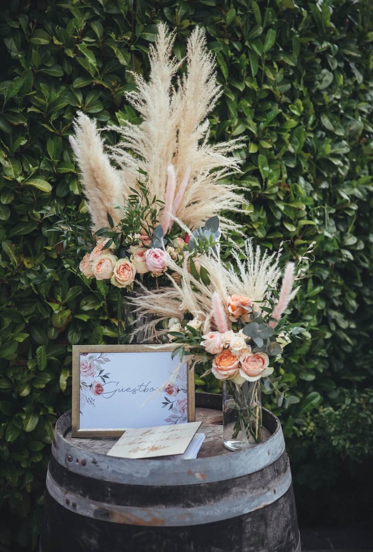 Wedding Flowers with roses and pampas grass with gold framed sign on a wooden barrel