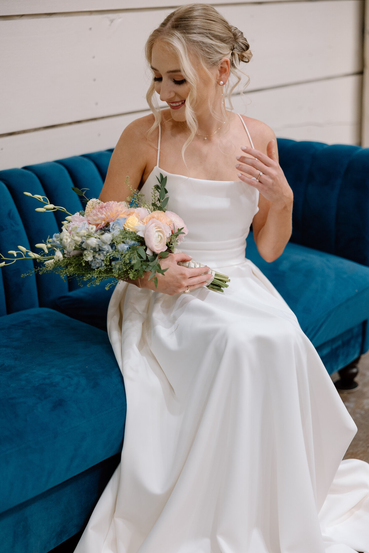 Bride sits on a blue velvet couch while she holds her bouquet.