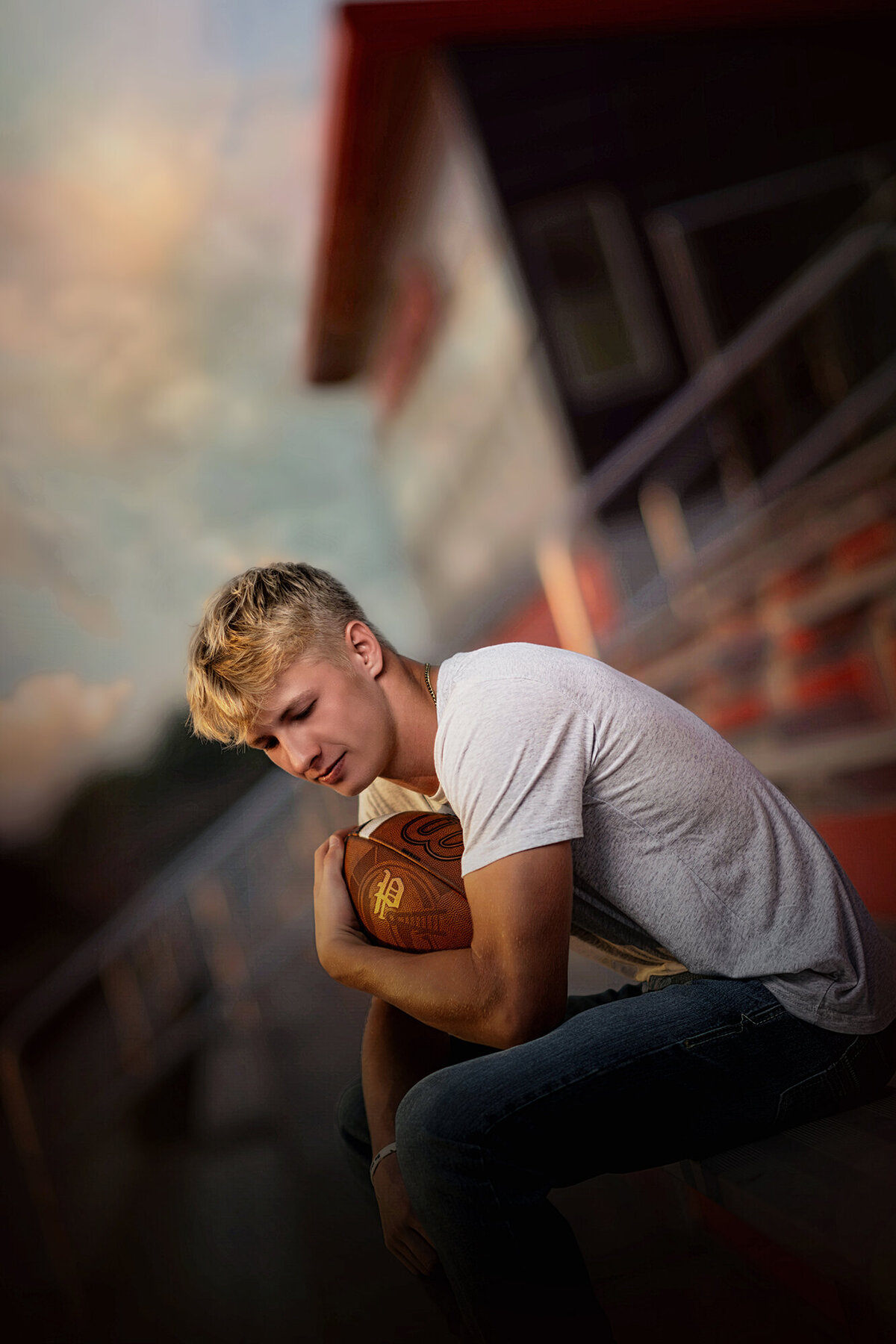 A Pella Senior Photographer captured image of a high school player sitting in the bleachers with a ball in his arm in grey shirt at sunset