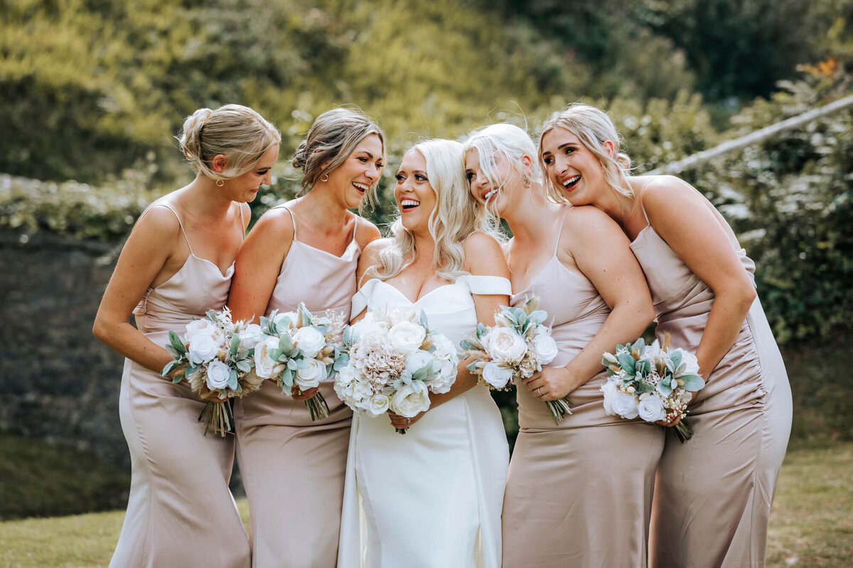 Bride and four bridesmaids standing in a garden holding bouquets and laughing