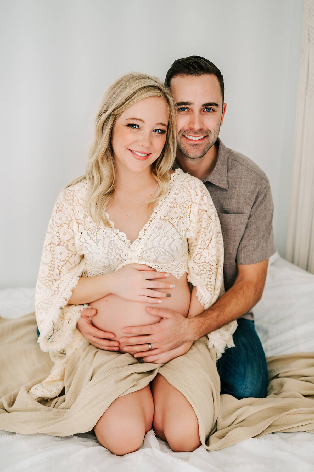 Springfield MO maternity photographer Jessica Kennedy of The XO Photography captures pregnant couple kneeling on bed smiling holding baby bump