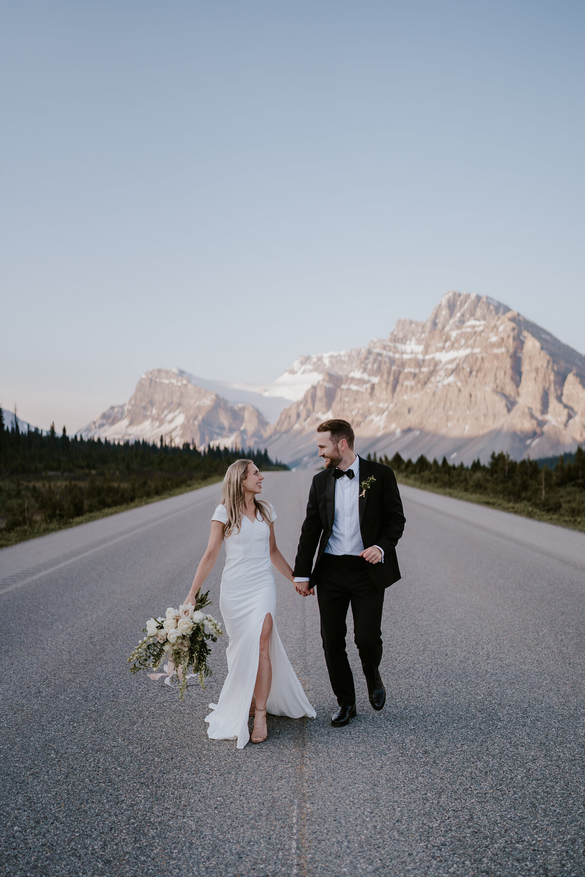 Bride and groom hold hands and run down the Icefield's Parkway at sunrise