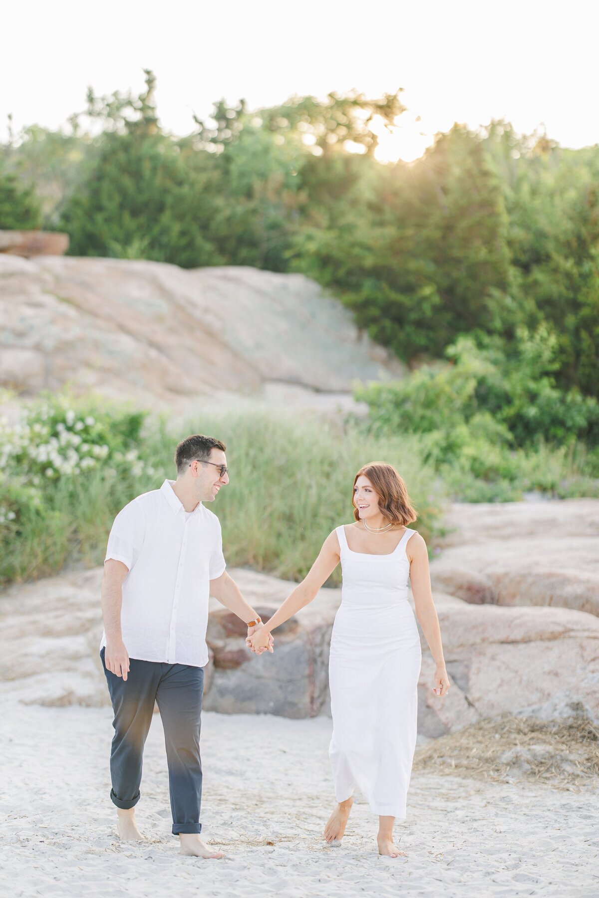 A couple holding hands and walking on Wingaersheek Beach during their engagement pictures.