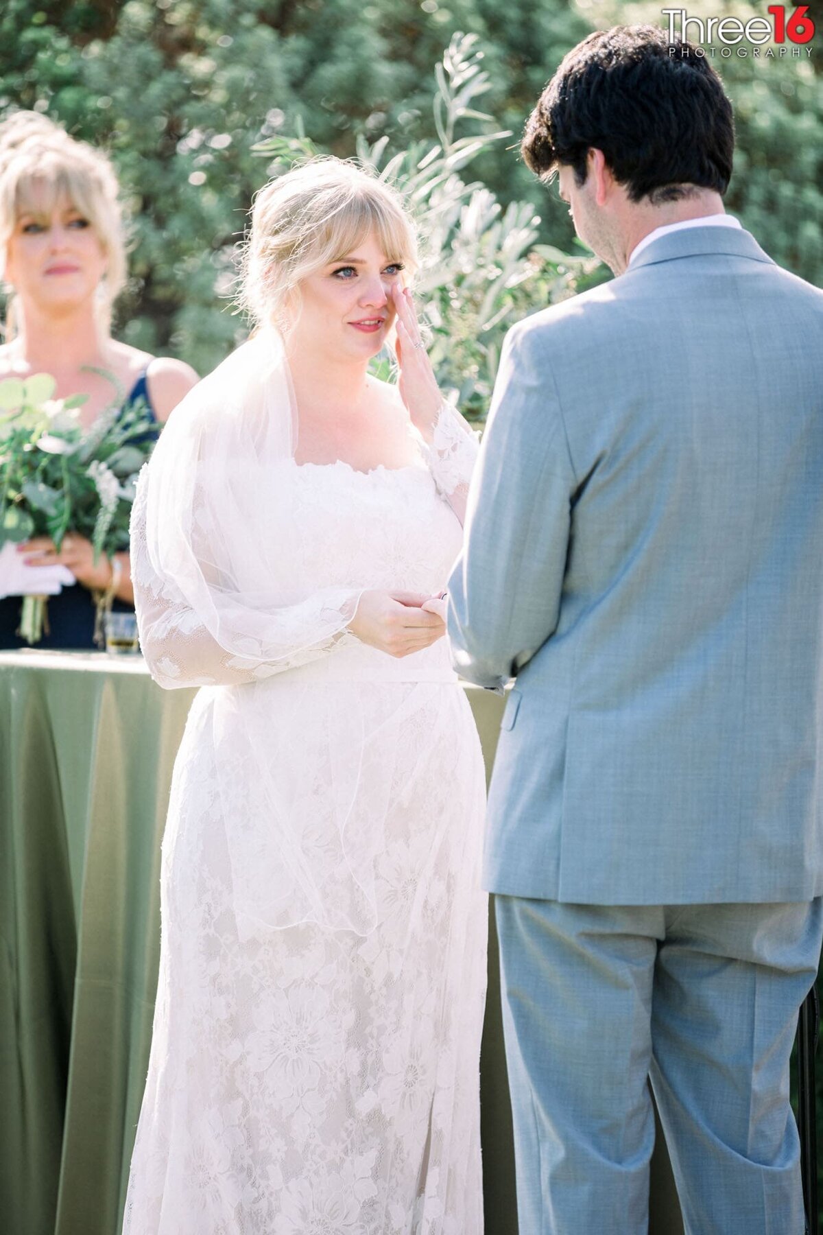 Bride wipes a tear from her cheek as her Groom reads his vows to her