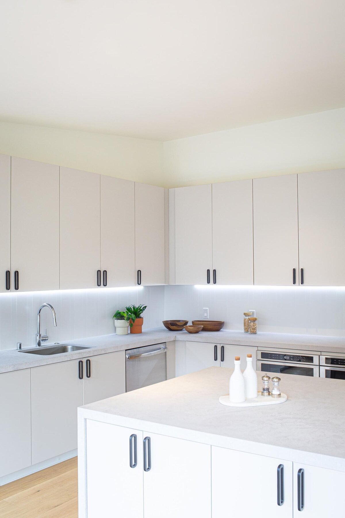 Bright, minimalist office kitchen with white cabinetry, under-cabinet lighting, and a central island with decor.