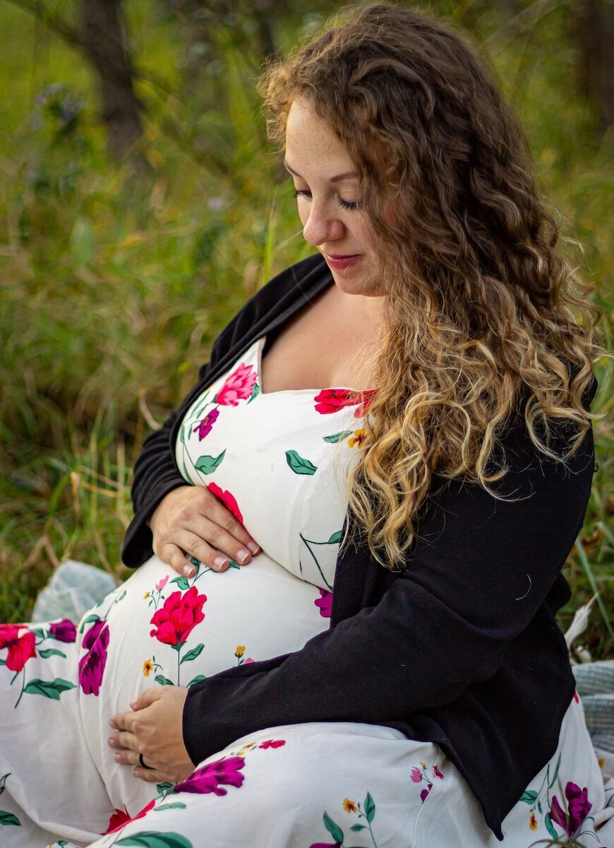 a pregnant woman sitting in a field  holding her pregnant belly near Edmonton