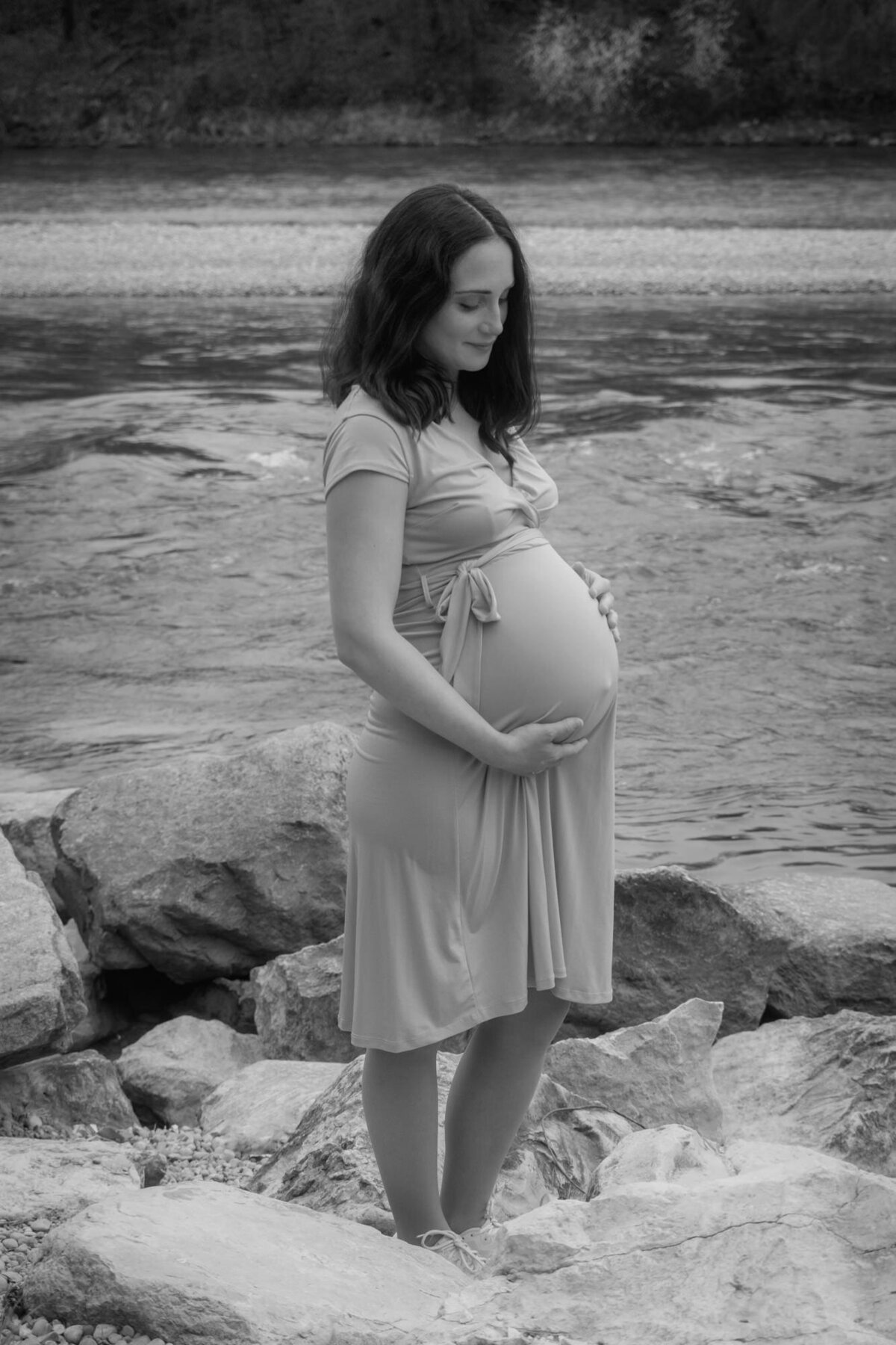 Maternity portrait of a woman standing in front of a lake, holding her bump.