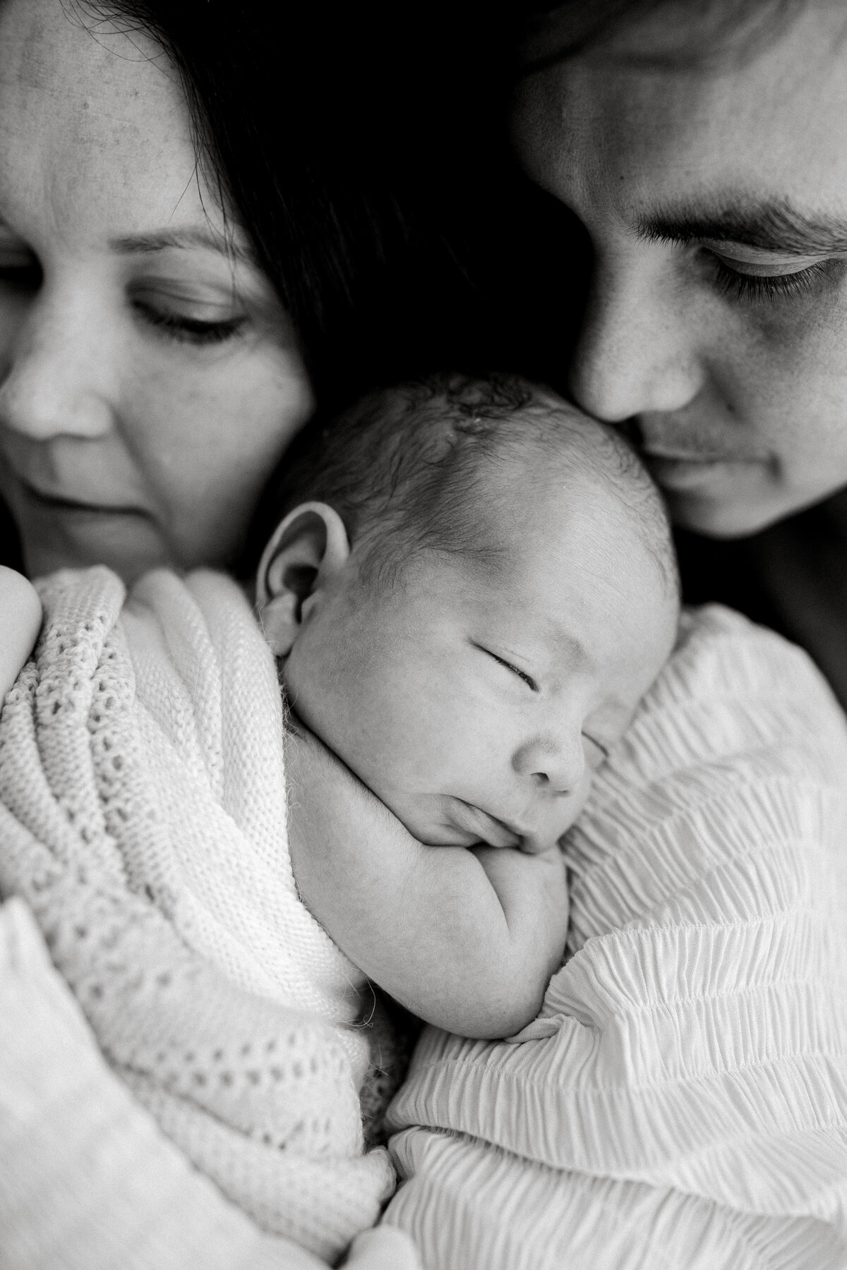A black and white photograph of a newborn child with her parents where they a looking at their newborn baby taken by newborn photographer lucy jane in christchurch