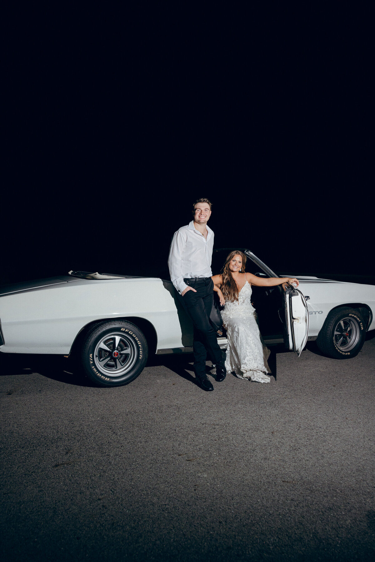 A wedding photo of the bride and groom posing with their getaway car at the end of the wedding reception