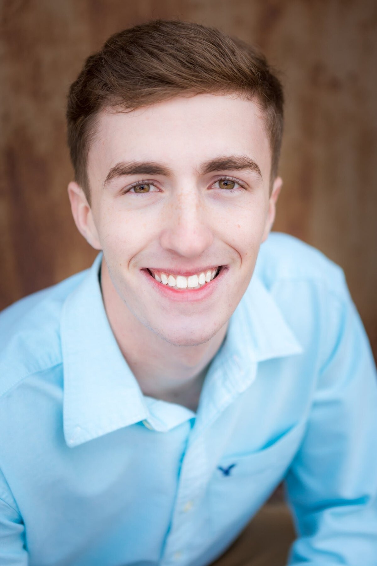 Handsome senior portrait of a guy wearing a blue shirt smiling broadly.