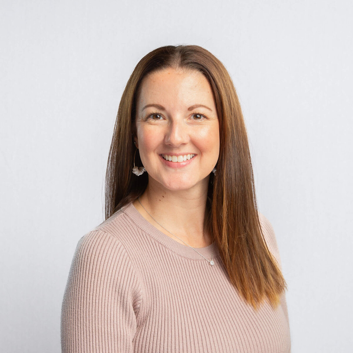 Headshot portrait of a woman with brown hair and a neutral top, in front of a light grey backdrop.