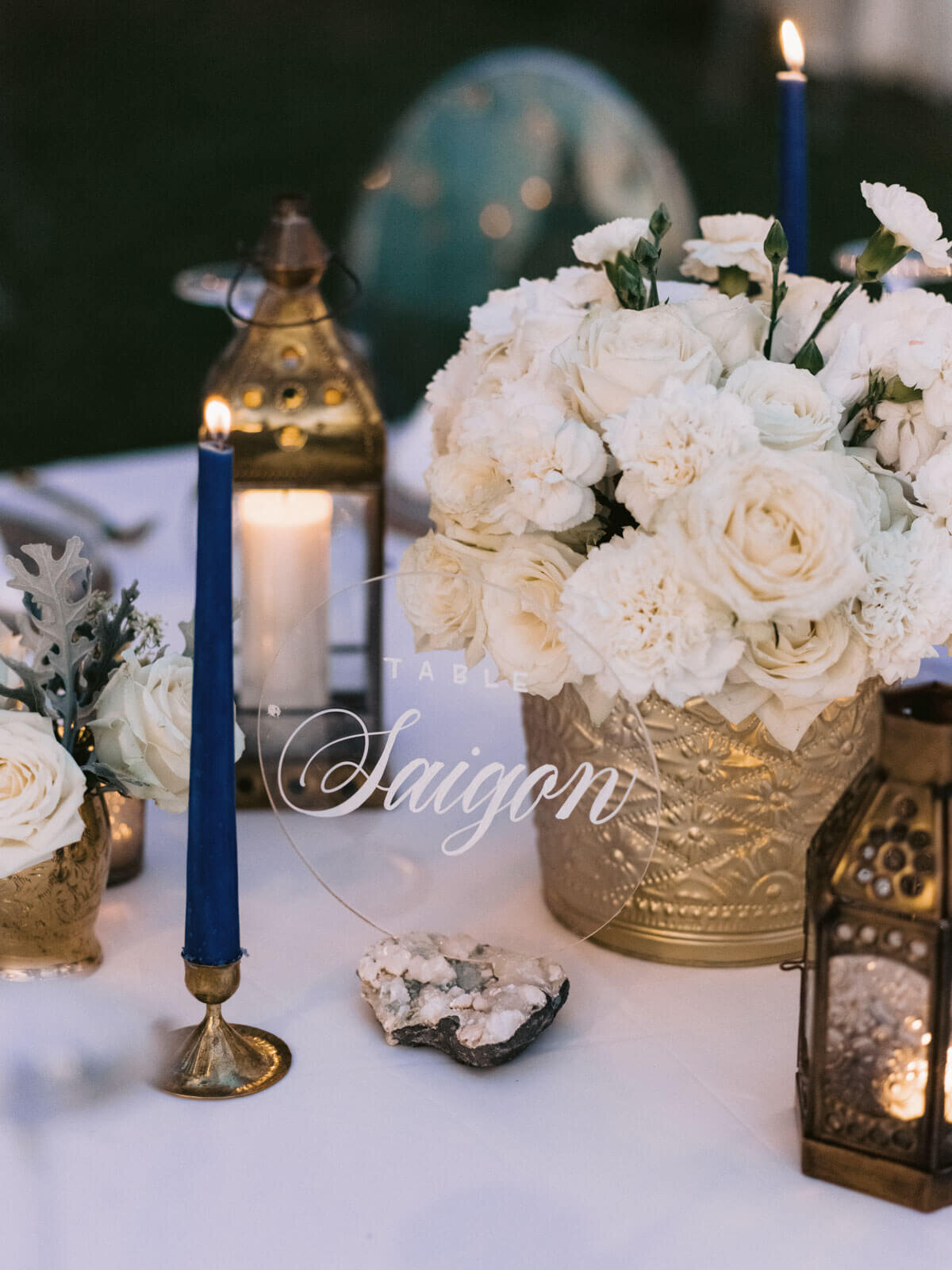 A table centerpiece of white flowers and candles on copper antique wares for a wedding in Khayangan Estate, Indonesia. Image by Jenny Fu Studio