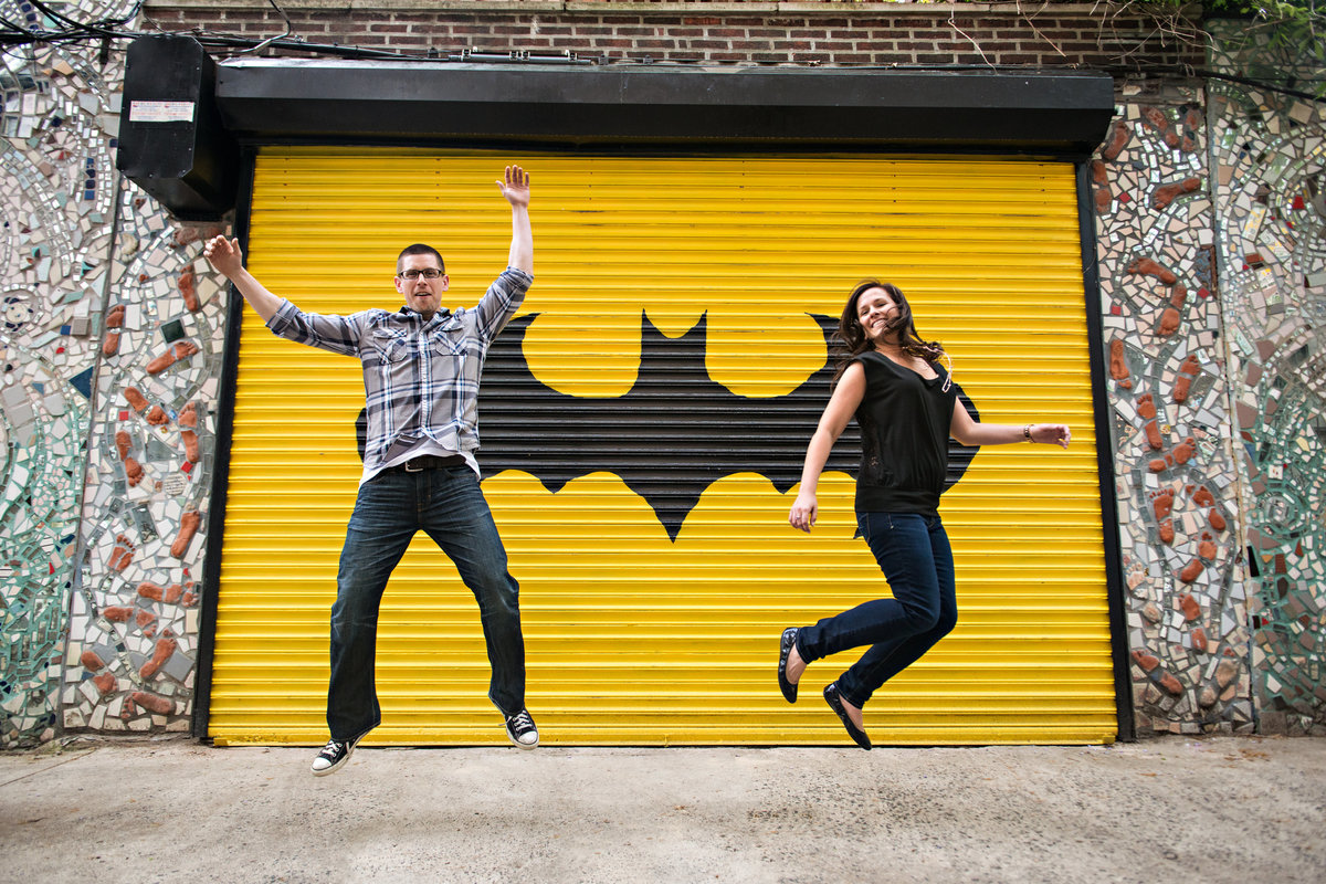 Engaged couple jump in front of a graffitied door on south street in philly.