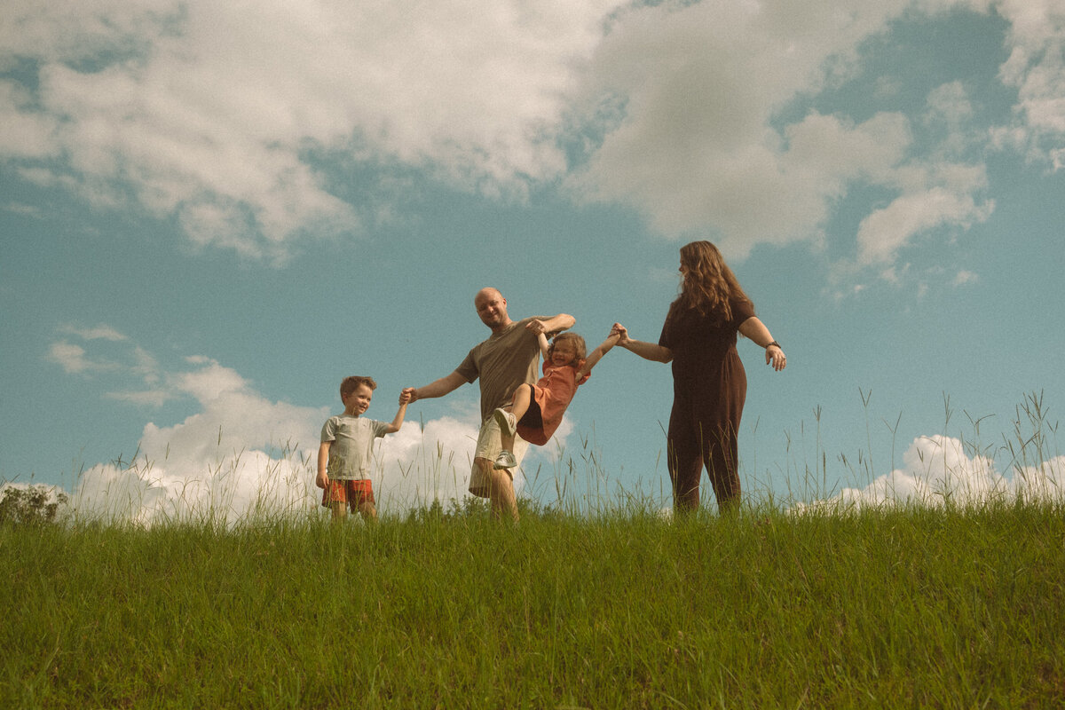 A family of four playing on a grass hill at Noonday Creek Trail on a bright sunny day. 