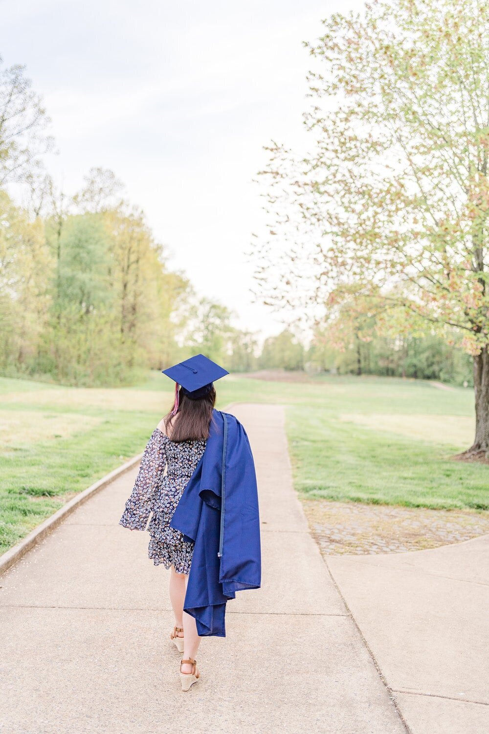 girl with graduation cap & gown walking away during senior photography in Northern Virginia