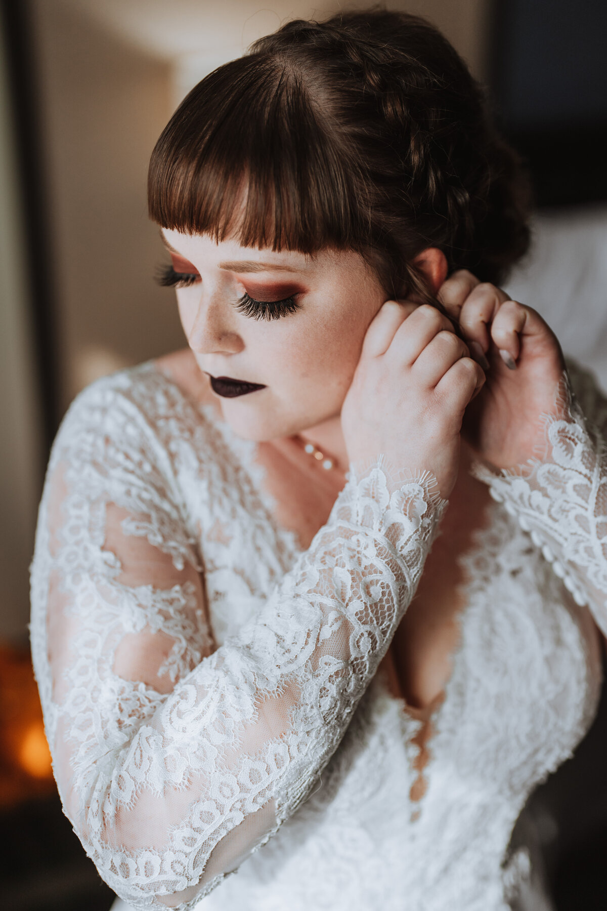 bride wearing lace dress and black lipstick putting on her earrings
