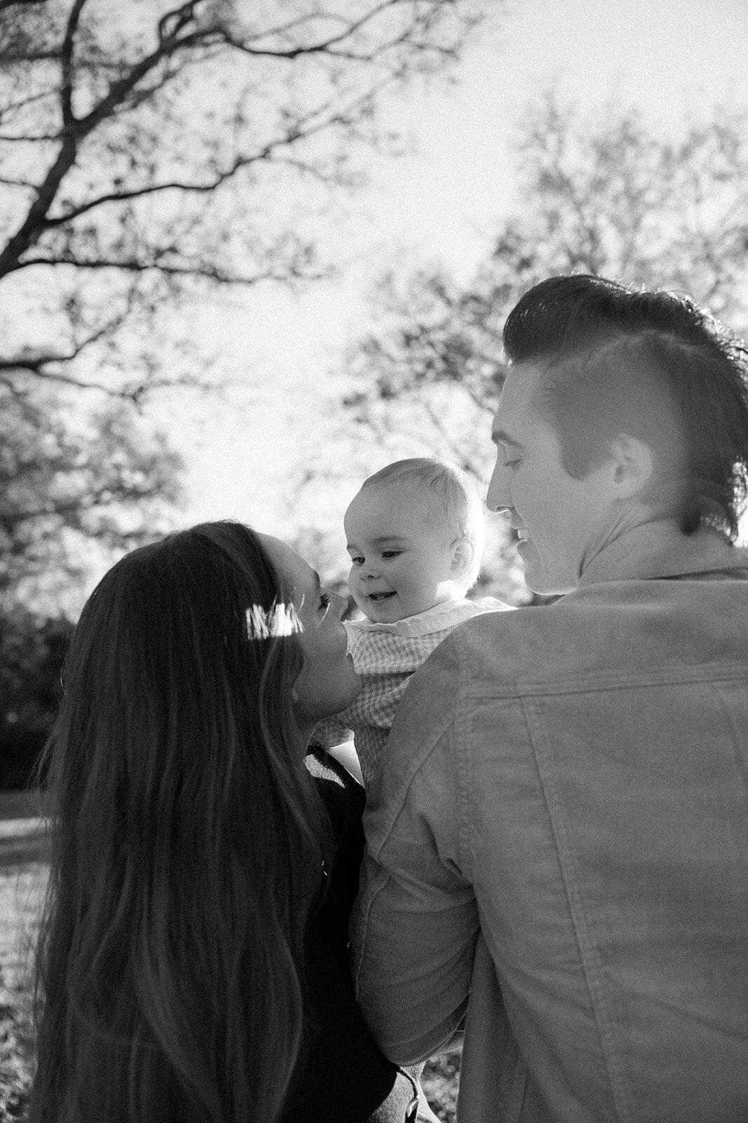 Mother lifts toddler over her shoulder in glow of golden hour as father stares at mother in awe. 