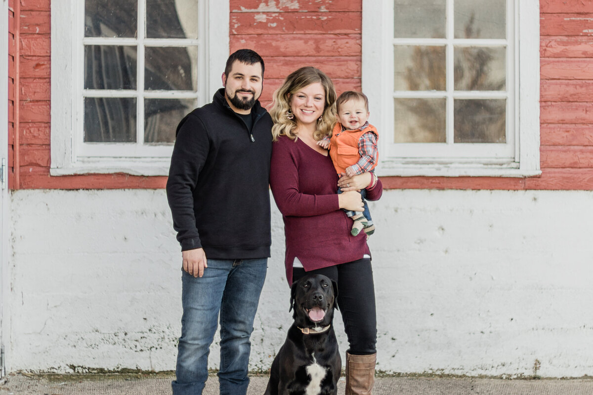 family standing with a dog in front of a barn